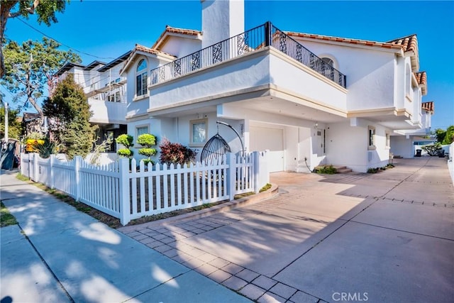 mediterranean / spanish-style house with stucco siding, a fenced front yard, a balcony, a tile roof, and driveway
