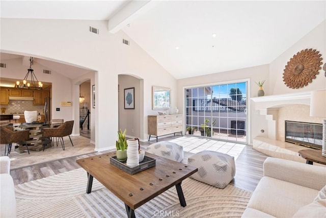 living room featuring light wood-style flooring, a chandelier, arched walkways, beamed ceiling, and high vaulted ceiling
