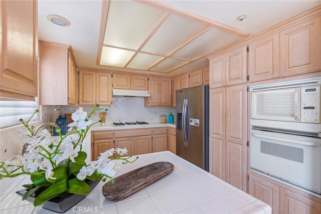 kitchen with white appliances, tile counters, under cabinet range hood, and light brown cabinets