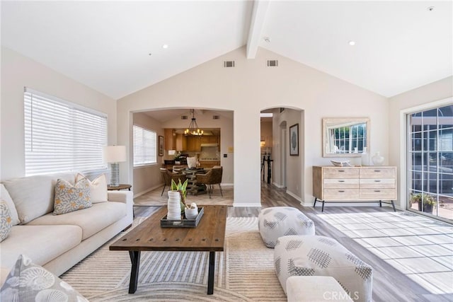 living room featuring arched walkways, a chandelier, beam ceiling, light wood finished floors, and baseboards