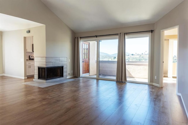 unfurnished living room with light wood finished floors, a tiled fireplace, baseboards, and high vaulted ceiling