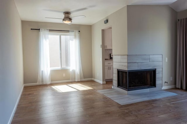 unfurnished living room featuring a ceiling fan, light wood-style floors, a tile fireplace, and baseboards