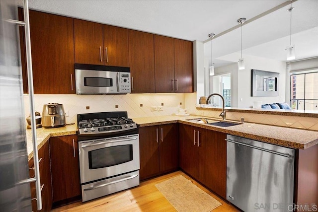 kitchen featuring appliances with stainless steel finishes, a sink, backsplash, a peninsula, and light wood-style floors