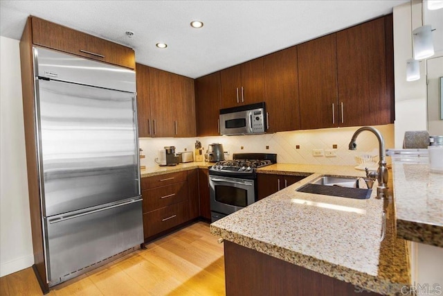 kitchen featuring stainless steel appliances, a sink, light wood-type flooring, light stone countertops, and recessed lighting