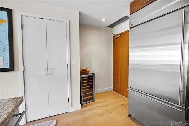 kitchen featuring stainless steel built in refrigerator, beverage cooler, light wood finished floors, recessed lighting, and baseboards