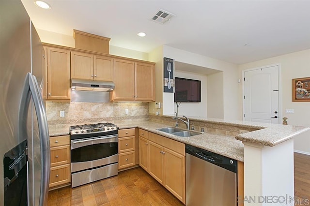kitchen featuring stainless steel appliances, under cabinet range hood, a peninsula, a sink, and light wood finished floors