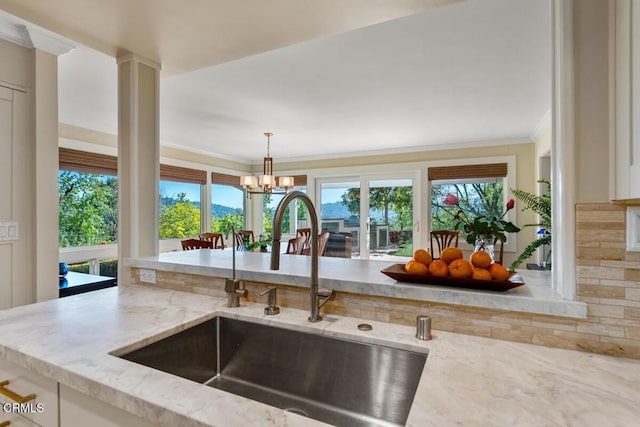 kitchen with a sink, crown molding, light stone counters, decorative light fixtures, and a chandelier