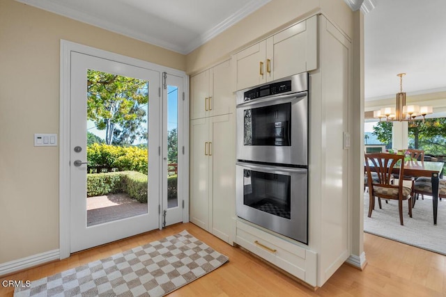 kitchen featuring stainless steel double oven, crown molding, a chandelier, light wood-type flooring, and white cabinetry
