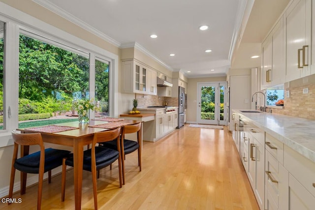 kitchen featuring a sink, wall chimney exhaust hood, ornamental molding, tasteful backsplash, and glass insert cabinets