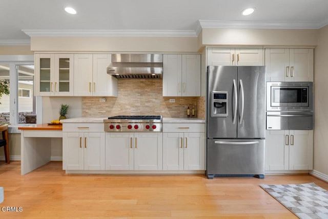 kitchen with stainless steel appliances, wall chimney range hood, a warming drawer, ornamental molding, and light countertops