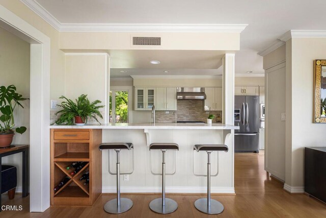 5109 Redwillow Ln, La Canada Flintridge, CA 91011 - kitchen featuring stainless steel refrigerator with ice dispenser, wall chimney range hood, a kitchen bar, light wood-style flooring, and light countertops