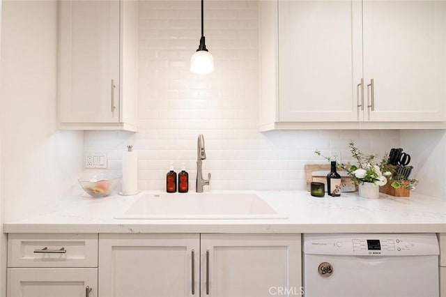 kitchen featuring white dishwasher, a sink, backsplash, light countertops, and white cabinets