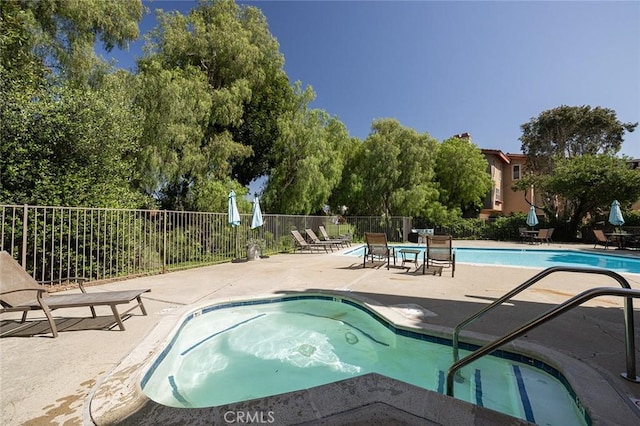 community pool with a patio area, fence, and a hot tub
