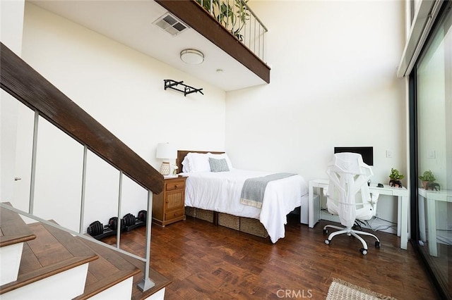 bedroom with wood finished floors, a towering ceiling, and an office area