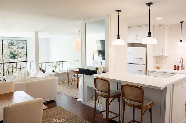 kitchen with freestanding refrigerator, dark wood-type flooring, white cabinetry, a breakfast bar area, and a sink