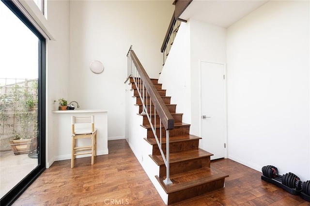 stairway featuring a towering ceiling, wood finished floors, and baseboards