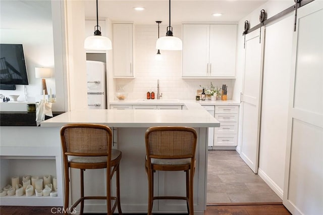 kitchen with freestanding refrigerator, a breakfast bar, backsplash, white cabinetry, and recessed lighting