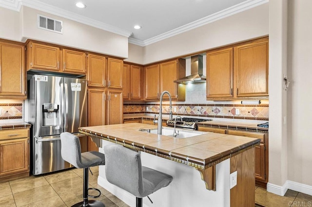 kitchen with stainless steel refrigerator with ice dispenser, wall chimney range hood, light tile patterned flooring, tile counters, and brown cabinets