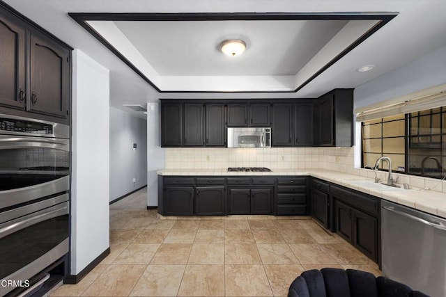 kitchen featuring stainless steel appliances, tasteful backsplash, a sink, tile countertops, and a tray ceiling