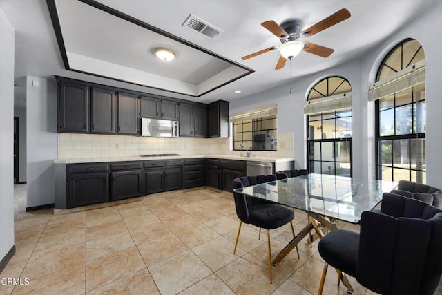 kitchen featuring appliances with stainless steel finishes, backsplash, ceiling fan, a raised ceiling, and a sink