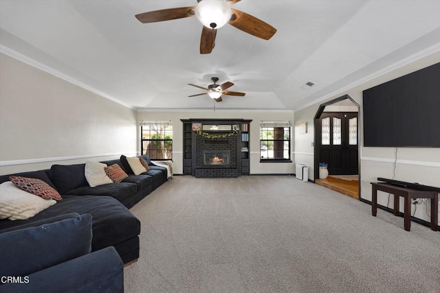 living area with healthy amount of natural light, carpet flooring, a ceiling fan, crown molding, and a brick fireplace