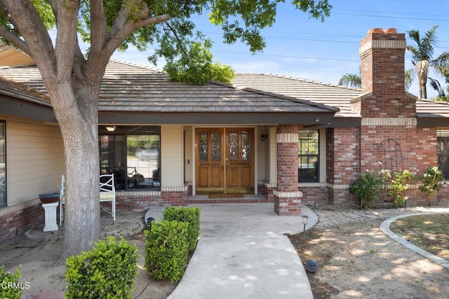 entrance to property with a chimney, brick siding, and a porch