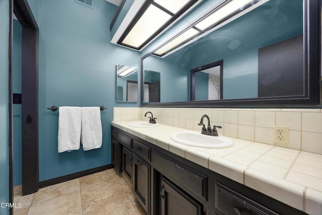 bathroom with backsplash, double vanity, baseboards, and stone finish flooring