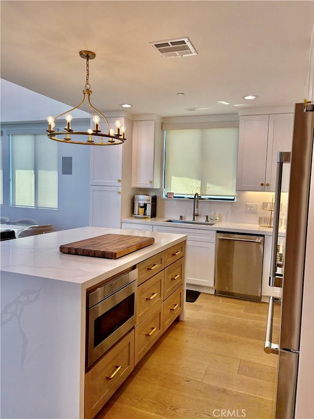 2621 Gates Ave Unit B, Redondo Beach, CA 90278 - kitchen with stainless steel appliances, a chandelier, white cabinets, light wood-style flooring, and hanging light fixtures