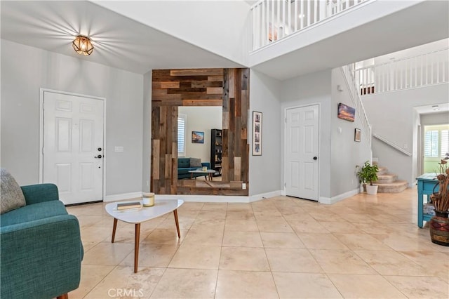 living room featuring a towering ceiling, light tile patterned flooring, baseboards, and stairway