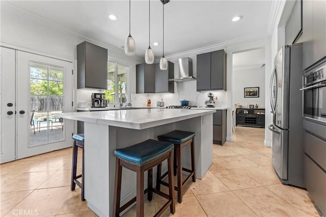kitchen featuring wall chimney range hood, stainless steel appliances, ornamental molding, light countertops, and a breakfast bar area