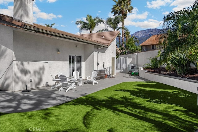 rear view of property with a mountain view, stucco siding, a patio area, a gate, and a tile roof