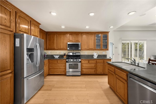 kitchen featuring stainless steel appliances, a sink, ornamental molding, brown cabinetry, and dark countertops