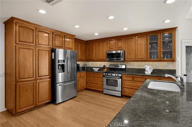kitchen featuring appliances with stainless steel finishes, a sink, brown cabinets, dark stone countertops, and recessed lighting
