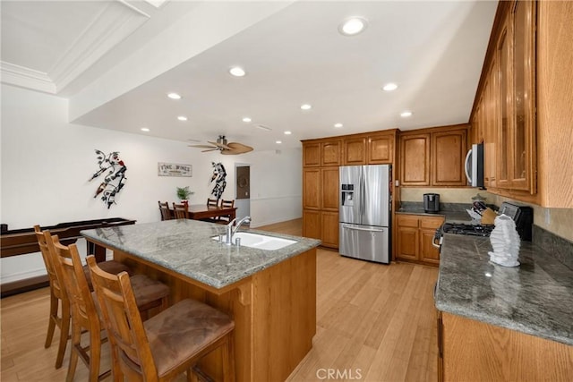 kitchen featuring appliances with stainless steel finishes, a sink, brown cabinets, recessed lighting, and light wood-style flooring