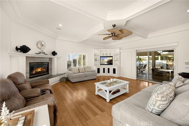 living area with coffered ceiling, ceiling fan, a glass covered fireplace, wood finished floors, and crown molding