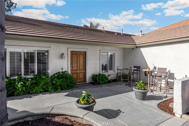 entrance to property with a tiled roof, stucco siding, and a patio
