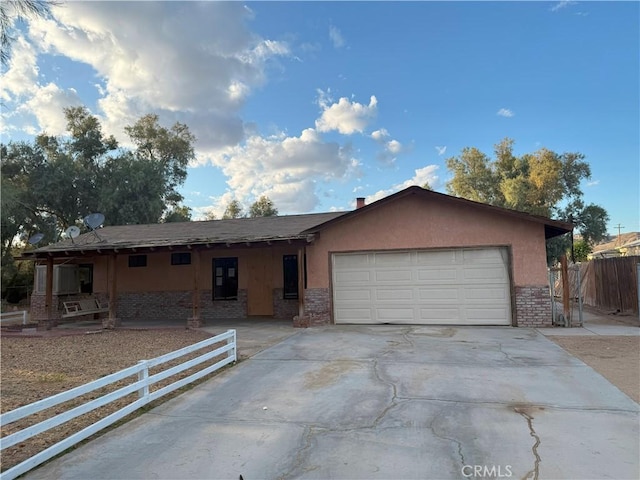 ranch-style home featuring a garage, brick siding, fence, concrete driveway, and stucco siding
