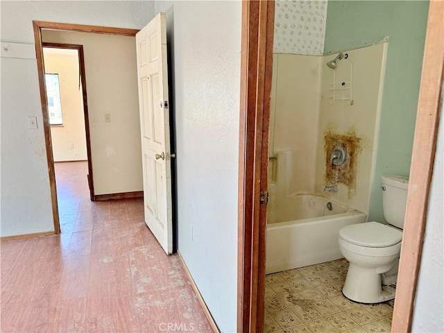 bathroom with toilet, shower / tub combination, and baseboards