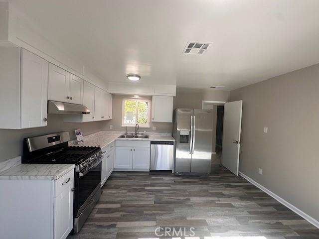 410 Orange Ave, Los Banos, CA 93635 - kitchen with appliances with stainless steel finishes, under cabinet range hood, white cabinets, light countertops, and dark wood-style flooring