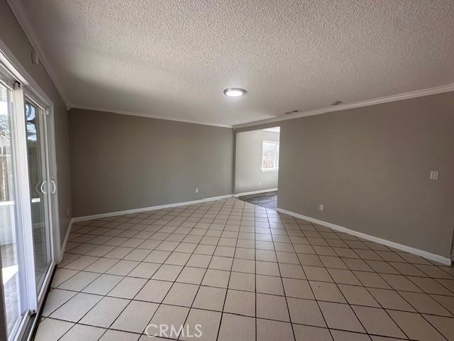 410 Orange Ave, Los Banos, CA 93635 - spare room with ornamental molding, a textured ceiling, baseboards, and light tile patterned flooring