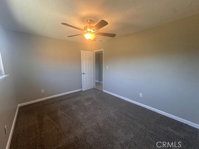 410 Orange Ave, Los Banos, CA 93635 - spare room with ceiling fan, dark carpet, and a textured ceiling