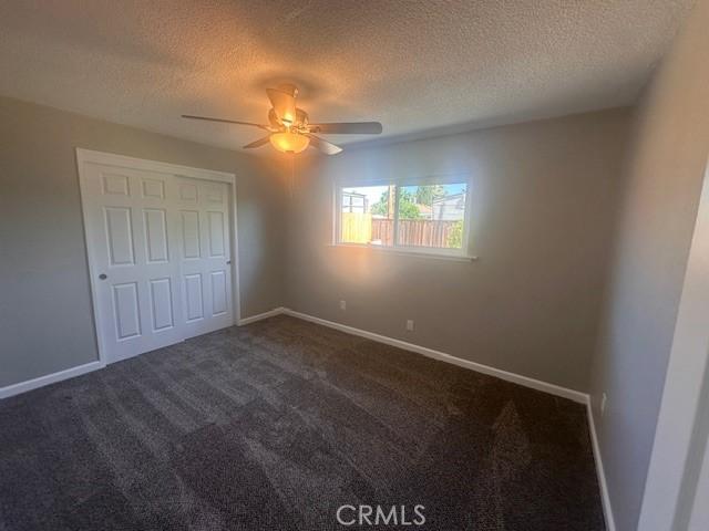 410 Orange Ave, Los Banos, CA 93635 - unfurnished bedroom featuring a textured ceiling, dark colored carpet, baseboards, and ceiling fan