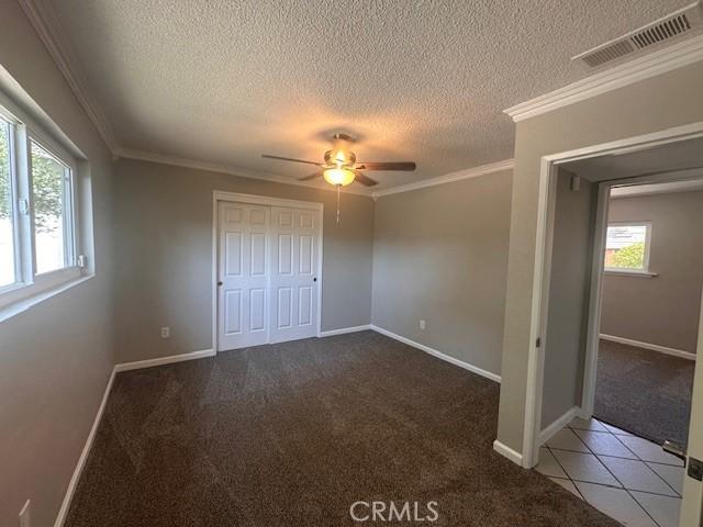 410 Orange Ave, Los Banos, CA 93635 - unfurnished bedroom featuring a textured ceiling, carpet, a closet, ornamental molding, and a ceiling fan