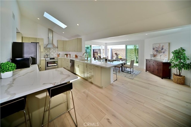 21651 Hilaria, Huntington Beach, CA 92646 - kitchen featuring a peninsula, wall chimney exhaust hood, appliances with stainless steel finishes, a kitchen breakfast bar, and a skylight