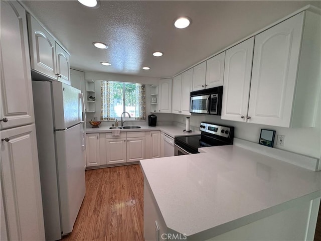 253 Calle Aragon Unit F, Laguna Woods, CA 92637 - kitchen featuring stainless steel appliances, open shelves, a sink, light wood finished floors, and a peninsula