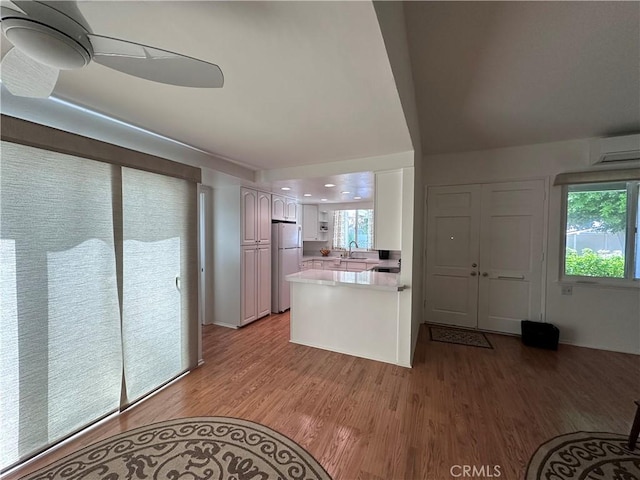 253 Calle Aragon Unit F, Laguna Woods, CA 92637 - kitchen featuring a wall mounted AC, white cabinetry, light wood finished floors, freestanding refrigerator, and a peninsula
