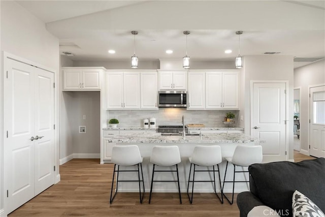 5122 Feather Rock Ct, Paradise, CA 95969 - kitchen featuring stainless steel microwave, a sink, white cabinets, tasteful backsplash, and a kitchen bar