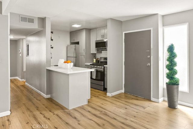 kitchen featuring stainless steel appliances, light wood finished floors, light countertops, and baseboards