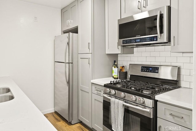kitchen with appliances with stainless steel finishes, tasteful backsplash, light countertops, light wood-style floors, and baseboards