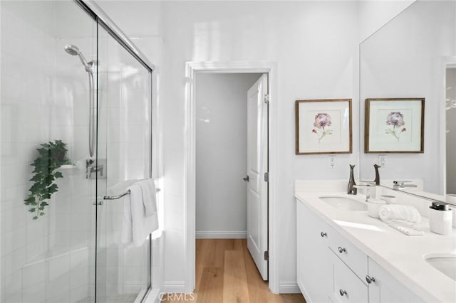 full bathroom with a stall shower, wood finished floors, double vanity, and baseboards